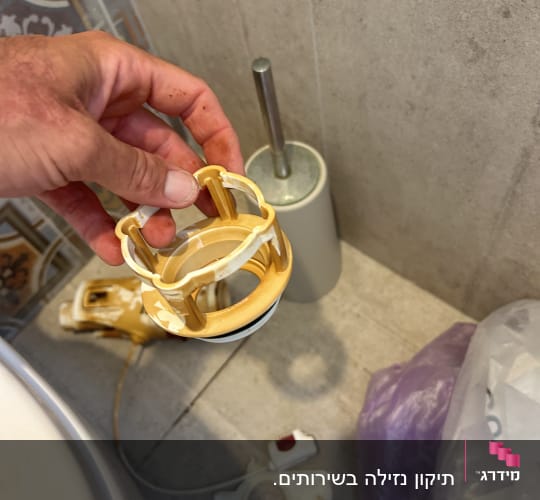 יד מחזיקה חלק פלסטיק צהוב ליד אסלה
